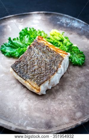 Gourmet fried European skrei cod fish filet with rapini broccoli rabe as closeup on a modern design plate 