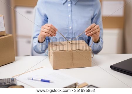 delivery, mail service, people and shipment concept - close up of woman packing parcel box and tying rope at post office