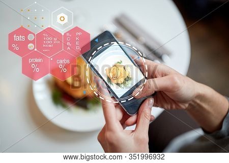 food, new nordic cuisine, technology, eating and people concept - close up of hands with breaded fish fillet on smartphone screen and nutritional value chart at restaurant