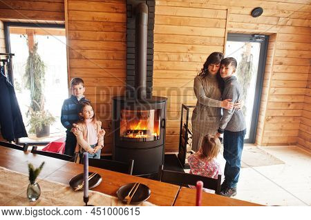 Mother And Four Kids In Modern Wooden House Against Table And Fireplace, Spending Time Together In W