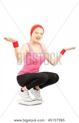 Happy young female standing on a weigth scale, isolated on white background