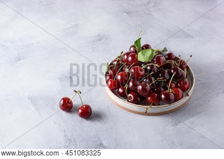 Berries Of Fresh Cherries In A Light Ceramic Plate On A Gray Concrete Background. Place For Text.