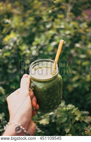 woman's hand holding a jar with green cold-pressed juice, nature background. Healthy eating, detoxing, juicing, body cleancing concept