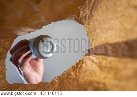 A Hand Retrieves A Gray Plastic Bottle In A Paper Bag. A Mature Man's Hand Holds A Sweet Ice Cream T