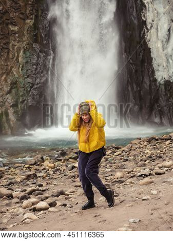 A Woman Stands Crouched And Laughing On The River Bank Against The Backdrop Of A Stormy Waterfall Fl