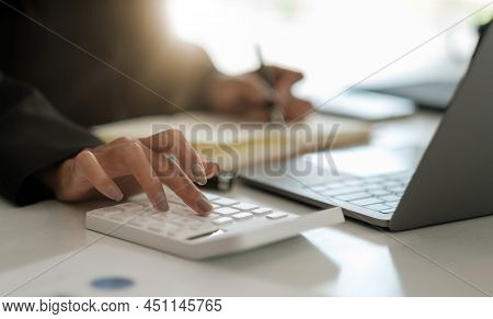Close Up Accountant Working On Desk In Office Using Calculator To Calculate Budget While Taking Note