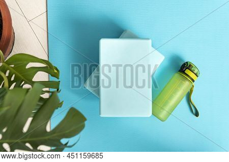 Top View Of Bluey Yoga Mat, Bottle With Water, Yoga Bricks And Green Plant. Workout At Home. Fitness