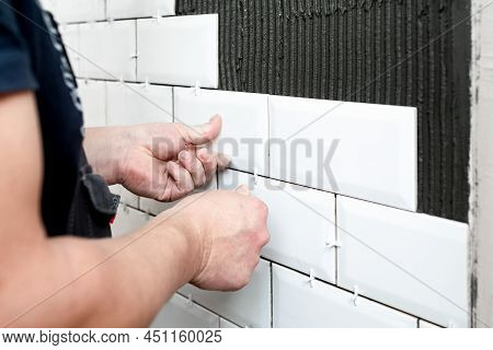 Workers Hands Installing Ceramic Tiles On The Kitchen Wall. A Handyman Using A Plastic Distance To A