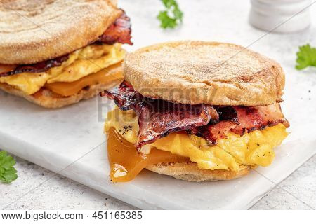 English Muffin, Scrumbled Egg, Ham, And Cheese Breakfast Sandwich On A Cutting Board