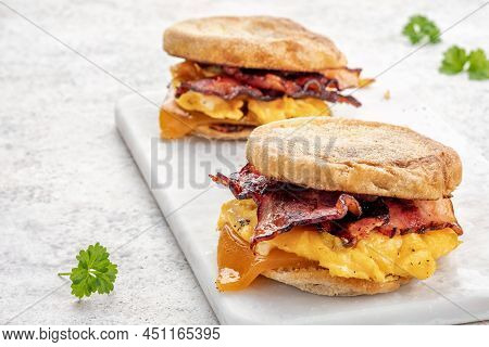 English Muffin, Scrumbled Egg, Ham, And Cheese Breakfast Sandwich On A Cutting Board