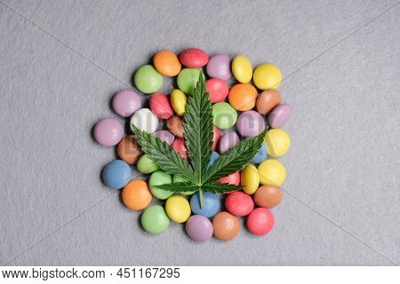 Cannabis Leaf With Colorful Candy Confetti Close Up. Marijuana Sweets With Cbd And Thc On Gray 
Back