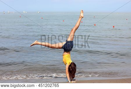 Slender Athletic Girl Barefoot On The Seashore While Effect The Rhythmic Gymnastics Exercises