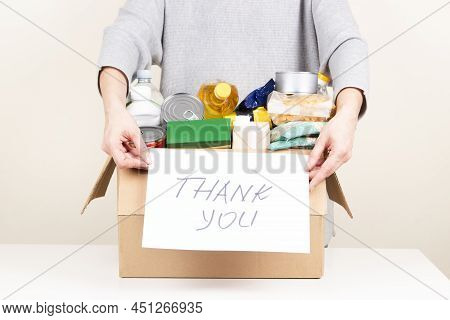Woman Hands Holding Cardbox With Grocery Products And Card With Inscription Thank You. Volunteer Col