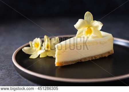 Classic New York Cheesecake With Fresh Vanilla Flower On Dark Concrete Background, Side View. A Piec
