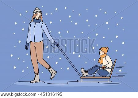 Happy Mother In Winterwear Ride Small Son On Sled Outdoors. Smiling Young Mom In Outerwear Relax Pla