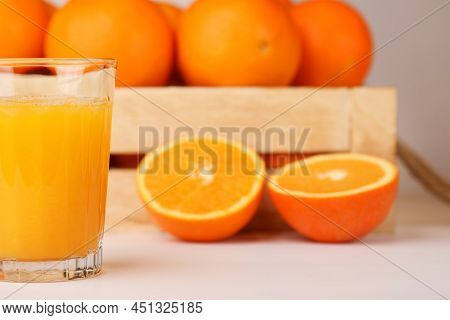 A Glass Of Fresh Orange Juice, Wooden Box With Rope Handles Full Of Fresh Oranges, Sliced Orange On 