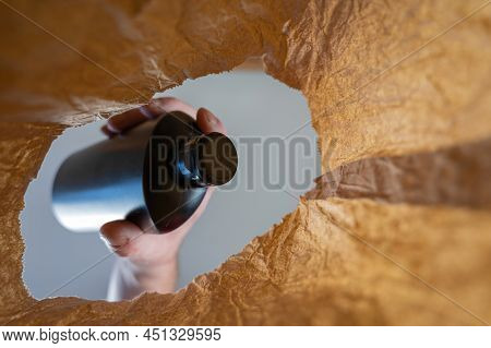 A Hand Places A Black Plastic Bottle From A Paper Bag. A Mature Man's Hand Holds A Bottle Of Shampoo