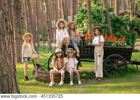 Preteen Girls Posing Near Old Wooden Cart Used As Flower Bed In Country Estate