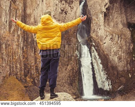 A Woman Stands With Her Hands Apart Against The Backdrop Of Steep Caucasian Rocks And A Waterfall. B