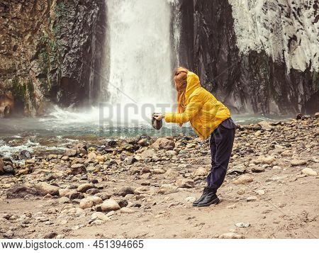 A Woman Stands Against The Backdrop Of A Stormy Waterfall Flowing Down From Wet, Icy Rocks, Filling 