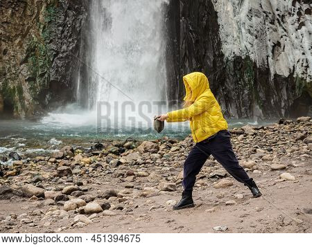 A Woman In A Yellow Jacket Stands Against The Background Of A Stormy Waterfall Flowing Down From Wet