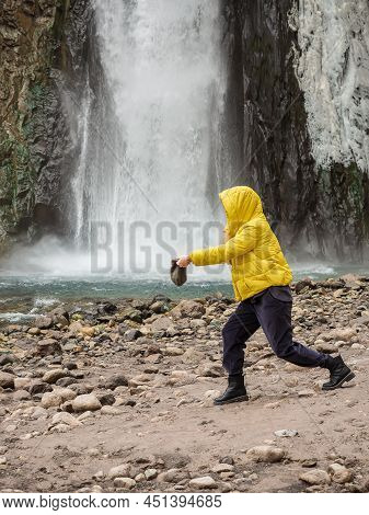 A Woman Stands On A Rocky Bank Of A River Against The Backdrop Of A Large Waterfall Flowing Down Fro