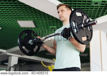 Athlete Man Lifting Barbells Working Out With Curl Bar In The Gym Doing Elevations. Caucasian Male T