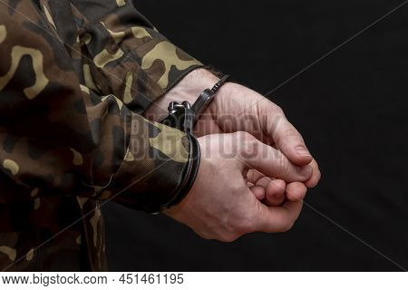 A military man in camouflage is handcuffed on a dark background. Concept: war criminal, prisoner of