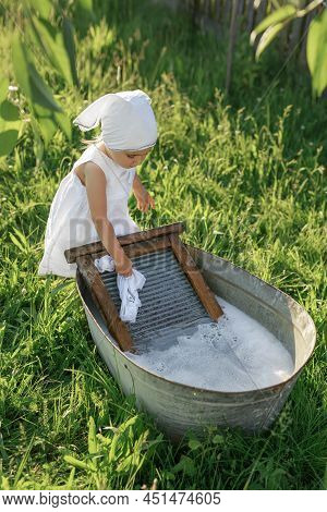 A Diligent Girl Helps Her Mom With Homework, Washing Clothes In A Basin In The Garden On A Washing B