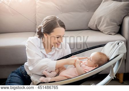 Happy Mother Playing With Girl Baby Lies In Automatic Carrycot, Sunlight At Home