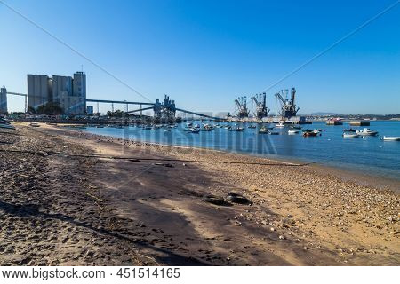 Trafaria; Portugal - March 01; 2022: Deep water terminal and silo for grain, derived products and oleaginous products in Trafaria, Portugal with fishing boats near the beach