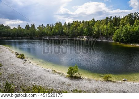 Panoramic Landscape View Over The Small Lake And Natural Surroundigs With A Beach And Woods Around T