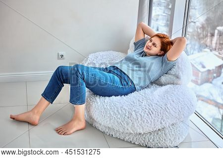 New Dwelling For Shoeless Woman Who Lies On Bean Bag Chair Near Floor To Ceiling Window.