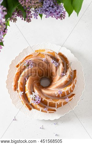 Lemon, Vanilla Bundt Cake With Sugar Glaze And Lilac Flowers On A White Background. Spring Compositi