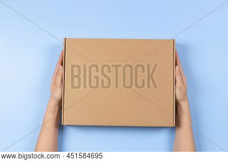 Top View To Female Hands Holding Brown Cardboard Box On Light Blue Background. Mockup Parcel Box. Pa