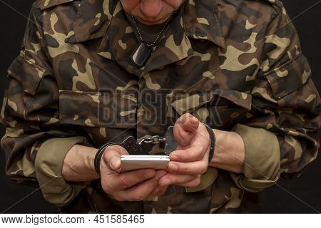 A Military Man In Handcuffs Makes A Phone Call On A Dark Background, Selective Focus. Concept: Priso