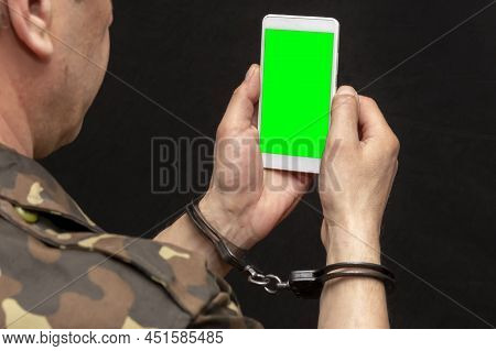 A Military Man In Handcuffs Makes A Phone Call On A Dark Background, Selective Focus. Concept: Priso