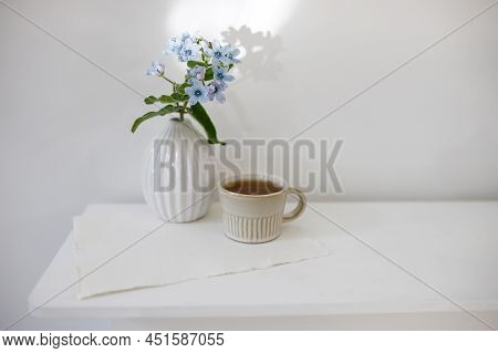 Flower Hackelia Velutina In A White Fluted Vase In The Style Of The Seventies And A Cup Of Coffee On