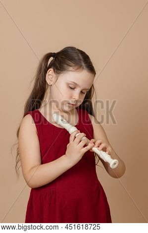 Girl In Red Dress Learn Melody By Pinching Holes In Flute With Bowed Head, Beige Background. Tuition