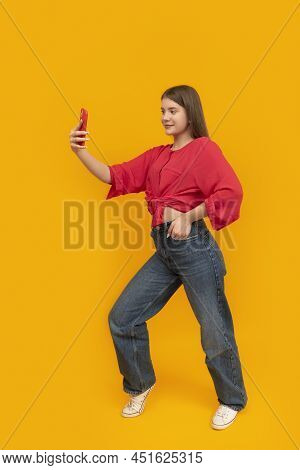 Portrait Of Teenage Girl In Red T-shirt And Jeans With Phone In The Studio On Yellow Background. You