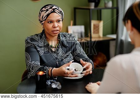 Portrait Of Female Fortune Teller Reading Coffee Grounds Telling Destiny In Seance With Young Woman,