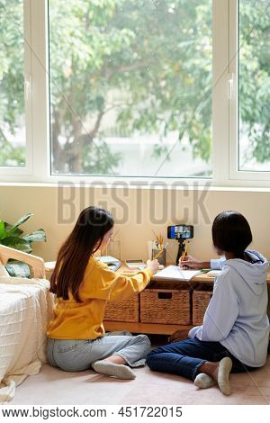 Teenage Girls Watching Online Lection On Smartphone And Writing In Notepad