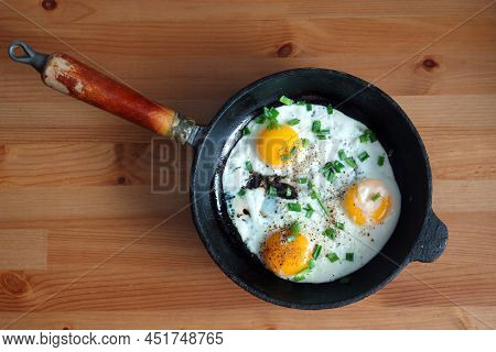 Fried Eggs Of Three Eggs On An Old Cast-iron Frying Pan Standing On Brown Wooden Table Top View Clos
