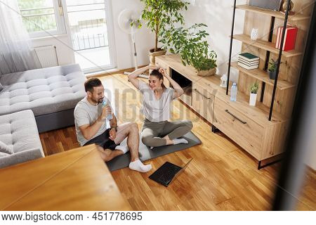 Couple Taking A Break While Doing Online Training Session Together At Home, Drinking Water And Getti