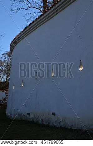 Defensive Wall Of The Castle With Loopholes. Zigzagging White Wall With Roof Tiles Roofing. Under Th