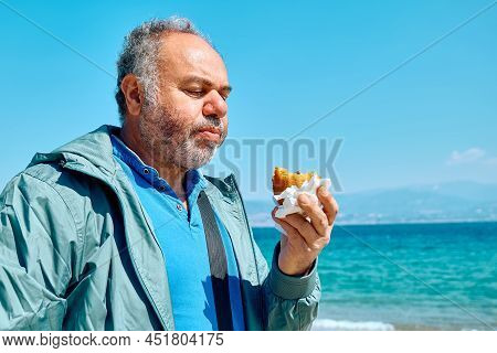 Bearded Mature Man At Spring Seaside Eating Hot Palatable Arancina (deep Fried Rice Balls With Meat)