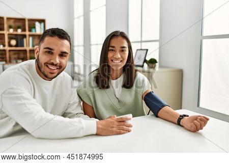 Young latin couple smiling happy measuring blood pressure using tensiometer at home.