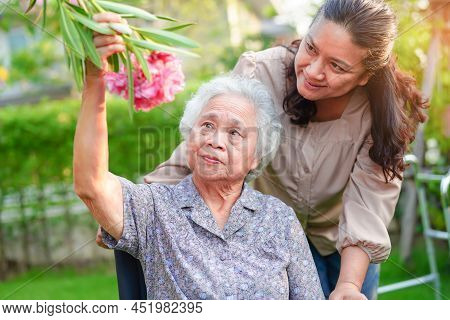 Asian Elderly Woman Enjoy In Flower Garden With Caregiver In Park.