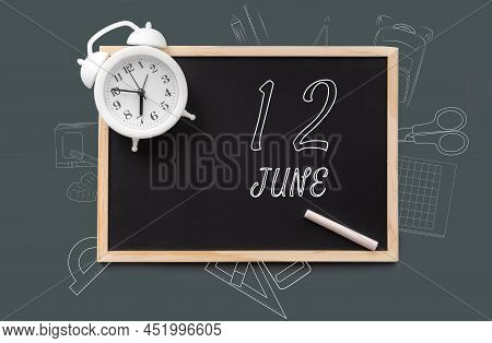 June 12. 12th Day Of Month, Calendar Date. Blackboard With Piece Of Chalk And White Alarm Clock On G