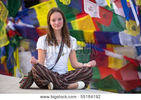 Girl sitting in the Lotus position on Buddhist stupa, prayer flags flying in the background.